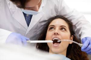 Dental professional in white coat and mask using intraoral camera or suction device on seated female patient